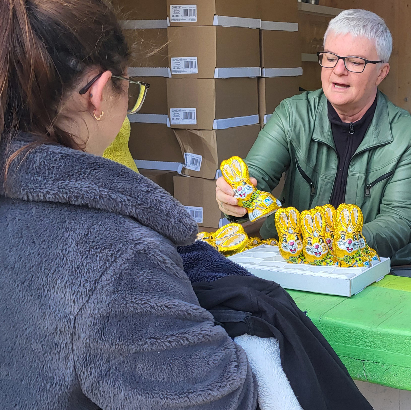 Two people at an outdoor market stand with golden chocolate Easter bunnies.