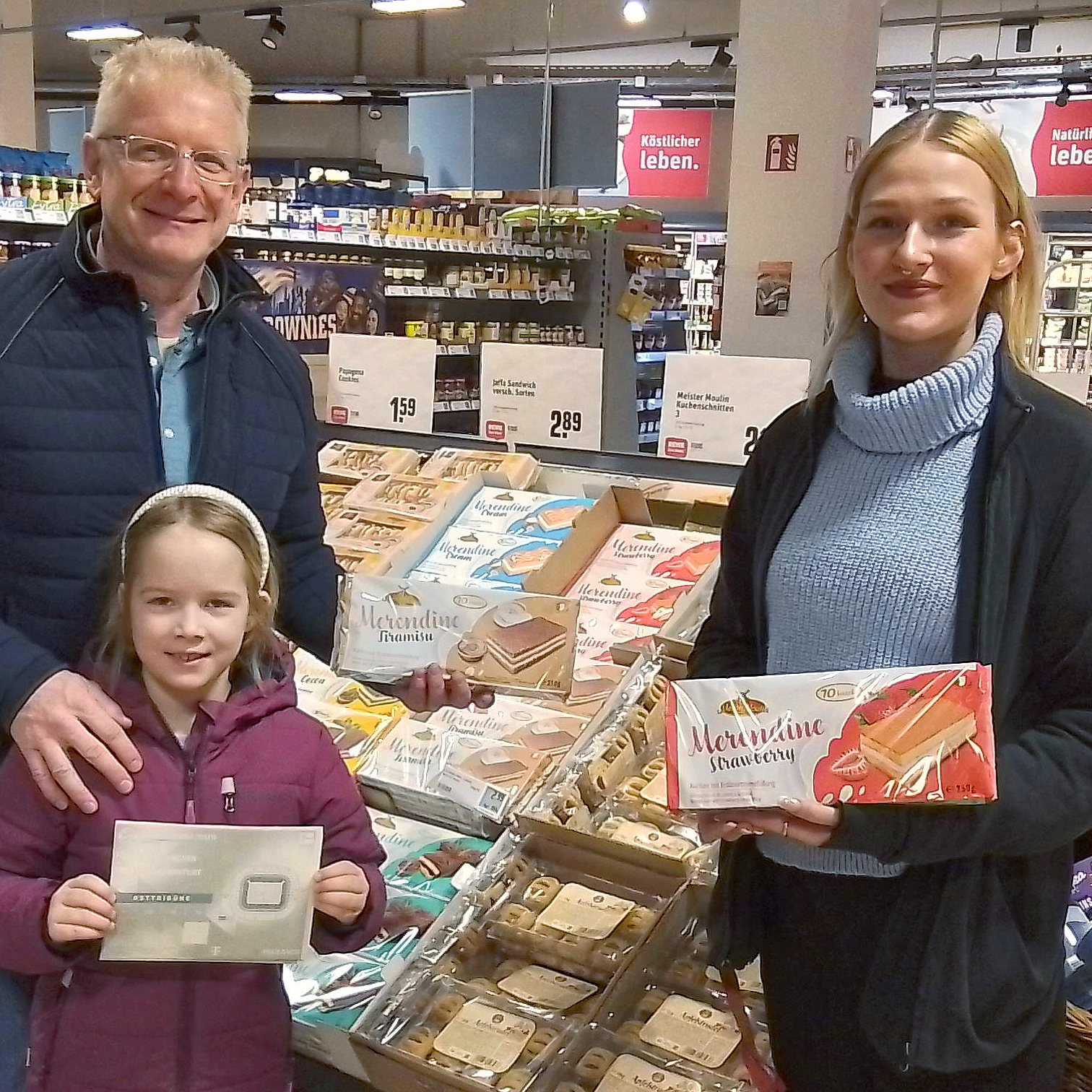 Three people in a supermarket presenting Merendine cakes and a voucher